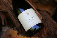 A bottle of Staindl Wines 2012 Pinot Noir rests on the bark of a log